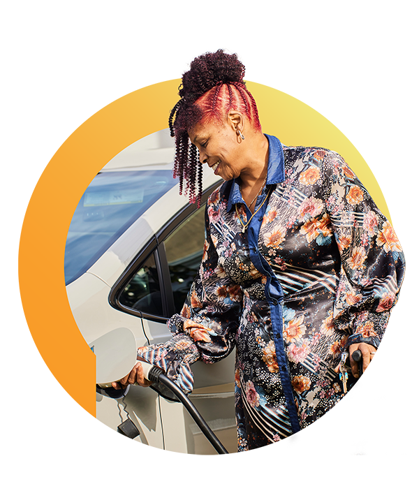 A woman in a floral jacket plugs a charging cable into an electric vehicle.