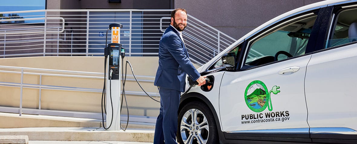 A man plugging an electric vehicle into a charging station.
