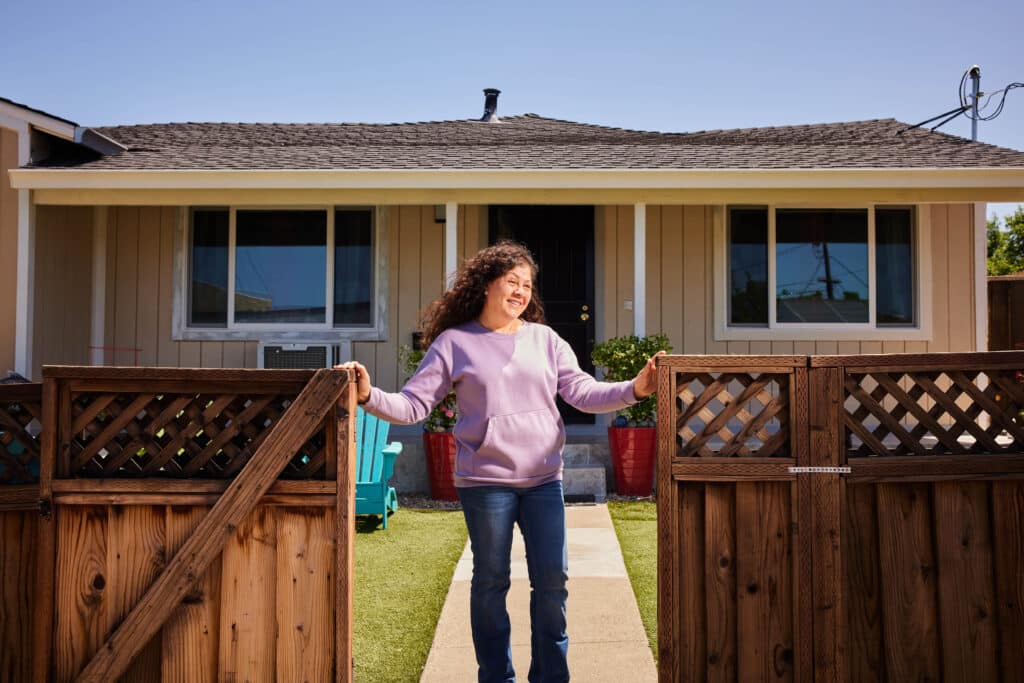 A person stands at the entrance to their property with a home in the background.
