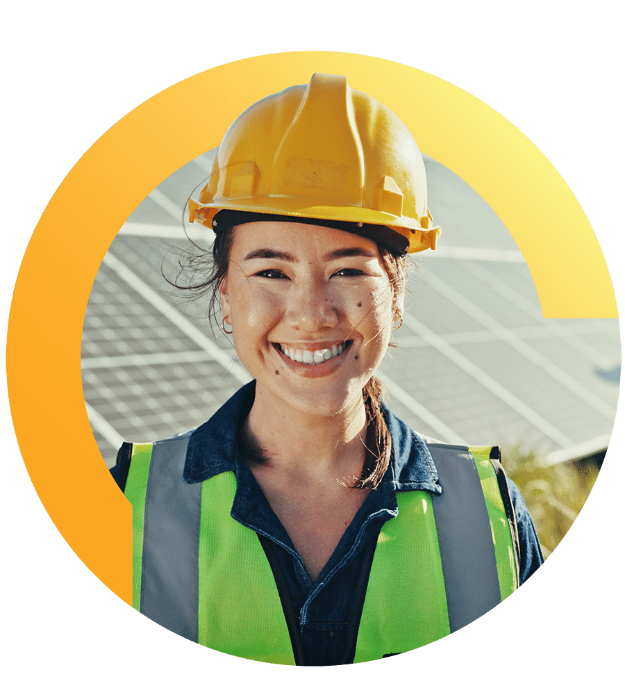 A worker in a hard hat and safety vest smiles in front of a solar panel installation.